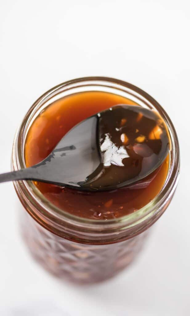 a spoon covered in sauce resting on the jar