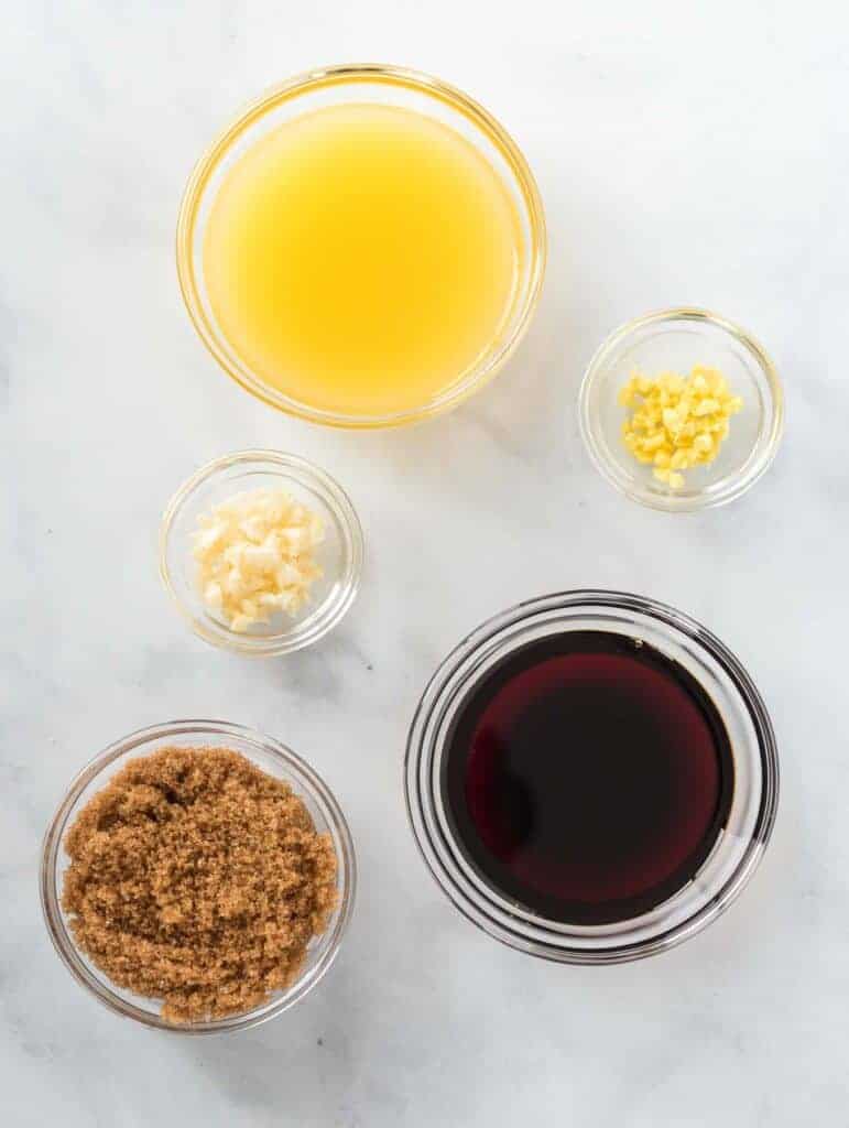 5 glass bowls filled with orange juice, garlic, ginger, brown sugar, and soy sauce