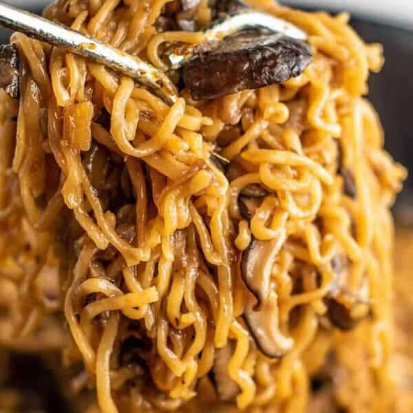 ramen noodles with mushrooms being pulled with tongs from a pan