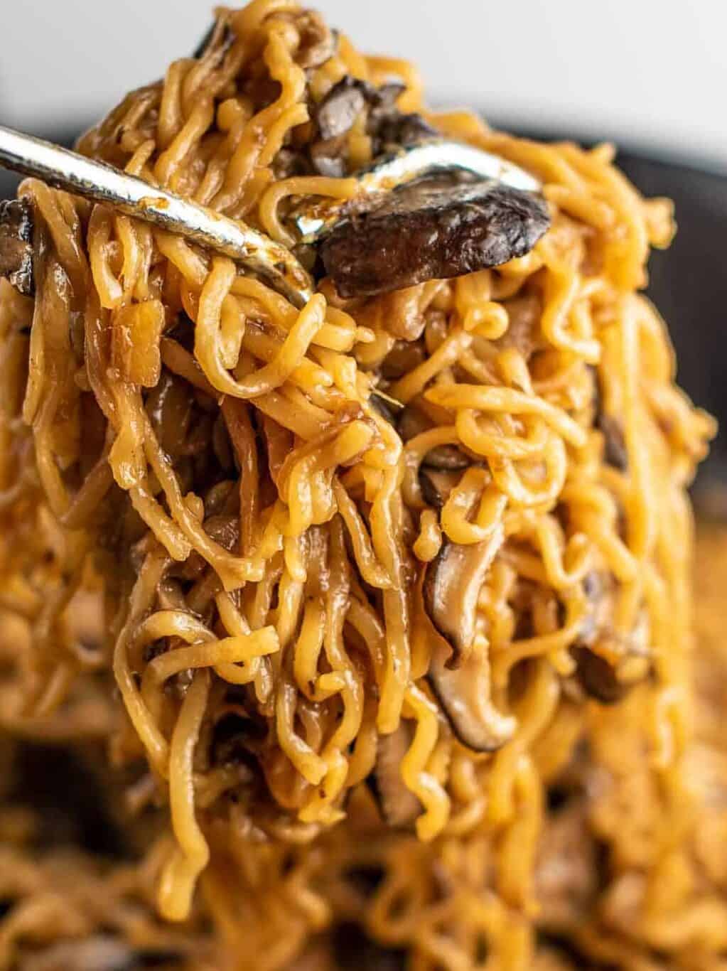 ramen noodles with mushrooms being pulled with tongs from a pan