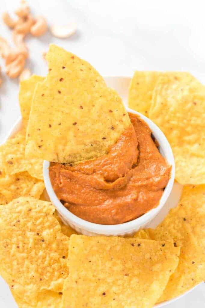 a chip dipped in a white ramekin of vegan queso