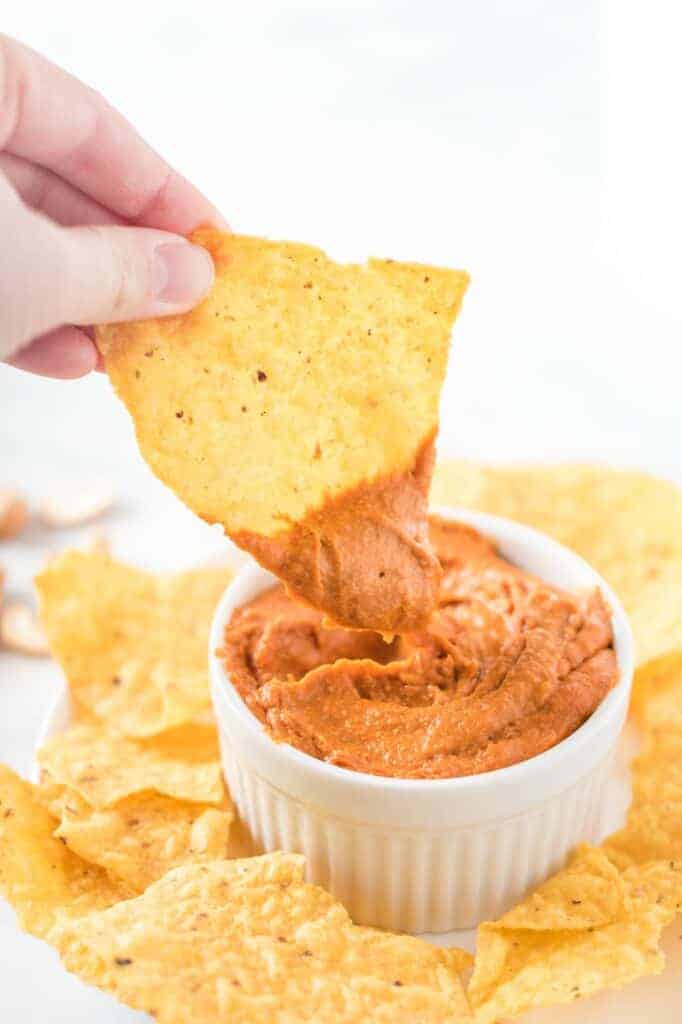 a chip dipped in a white ramekin of vegan queso