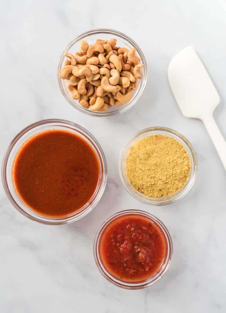 the ingredients in separate glass bowls (cashews, nutritional yeast, salsa, and enchilada sauce)