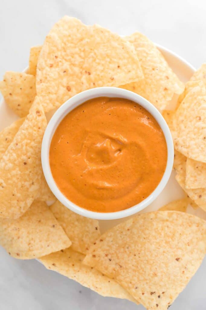 vegan queso in a white ramekin surrounded by tortilla chips