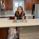 joy standing in her kitchen with a sign reading build your bite