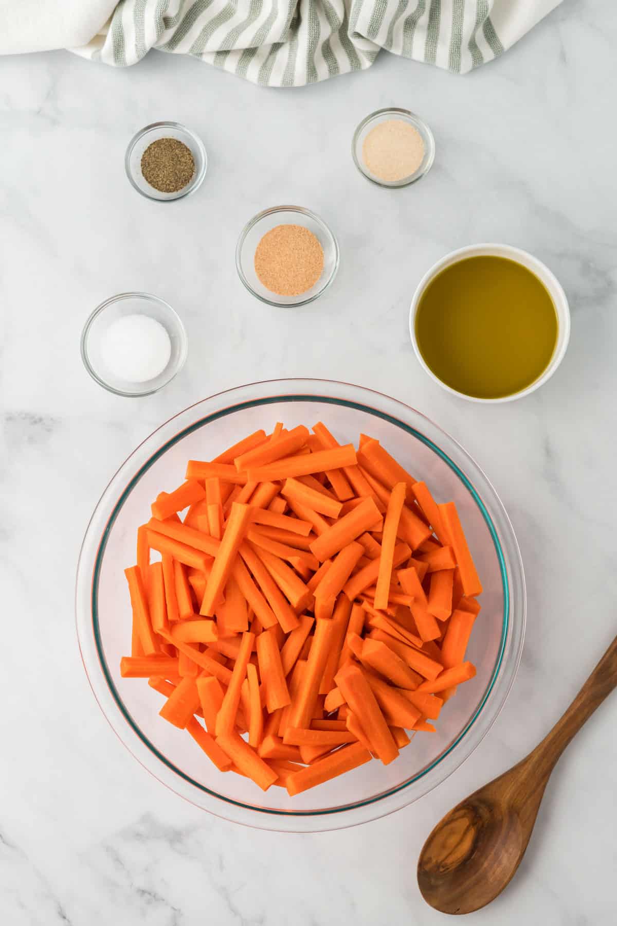 cut up carrots in a bowl with olive oil and spices in bowls next to it