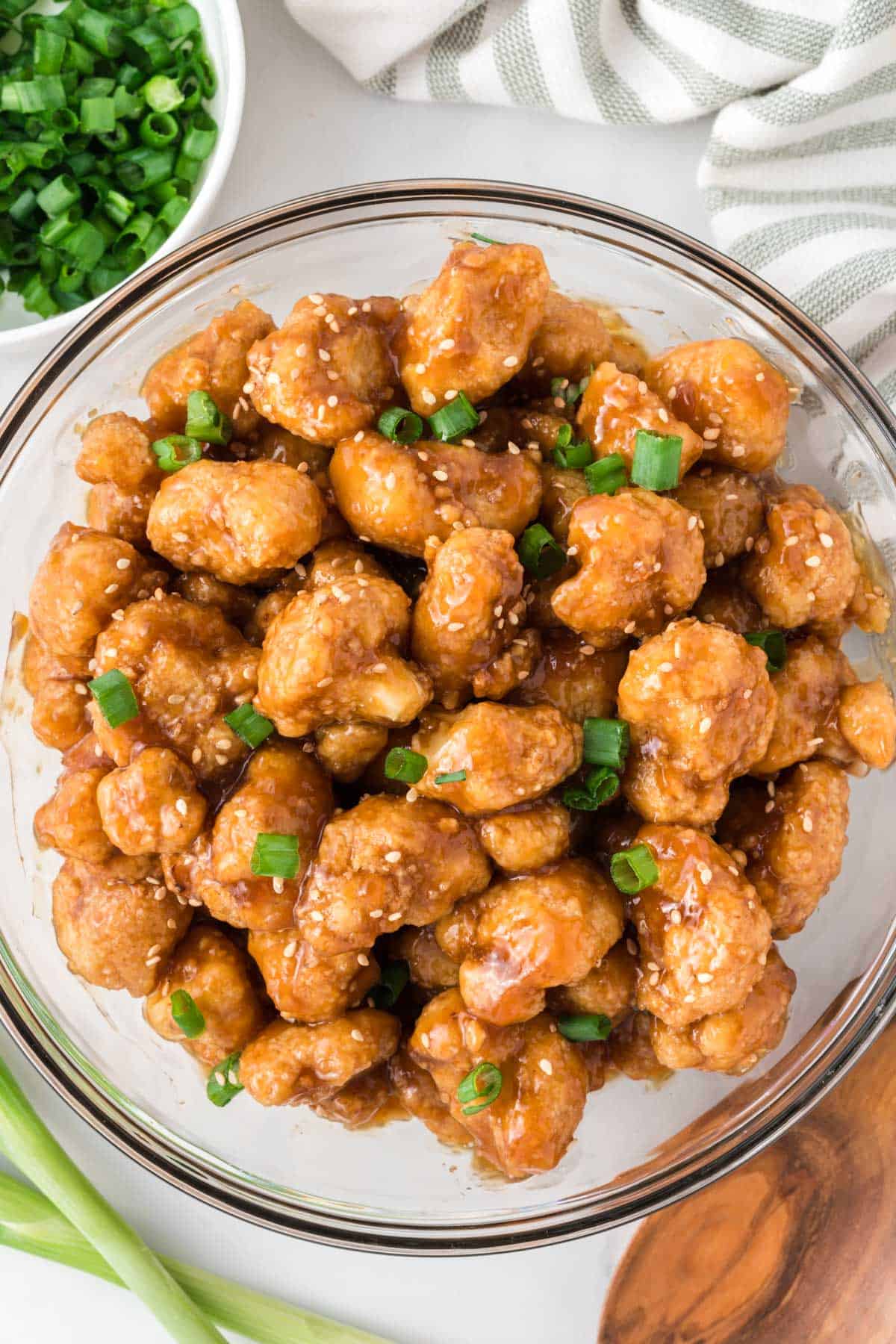 teriyaki cauliflower in a bowl topped with green onions and sesame seeds