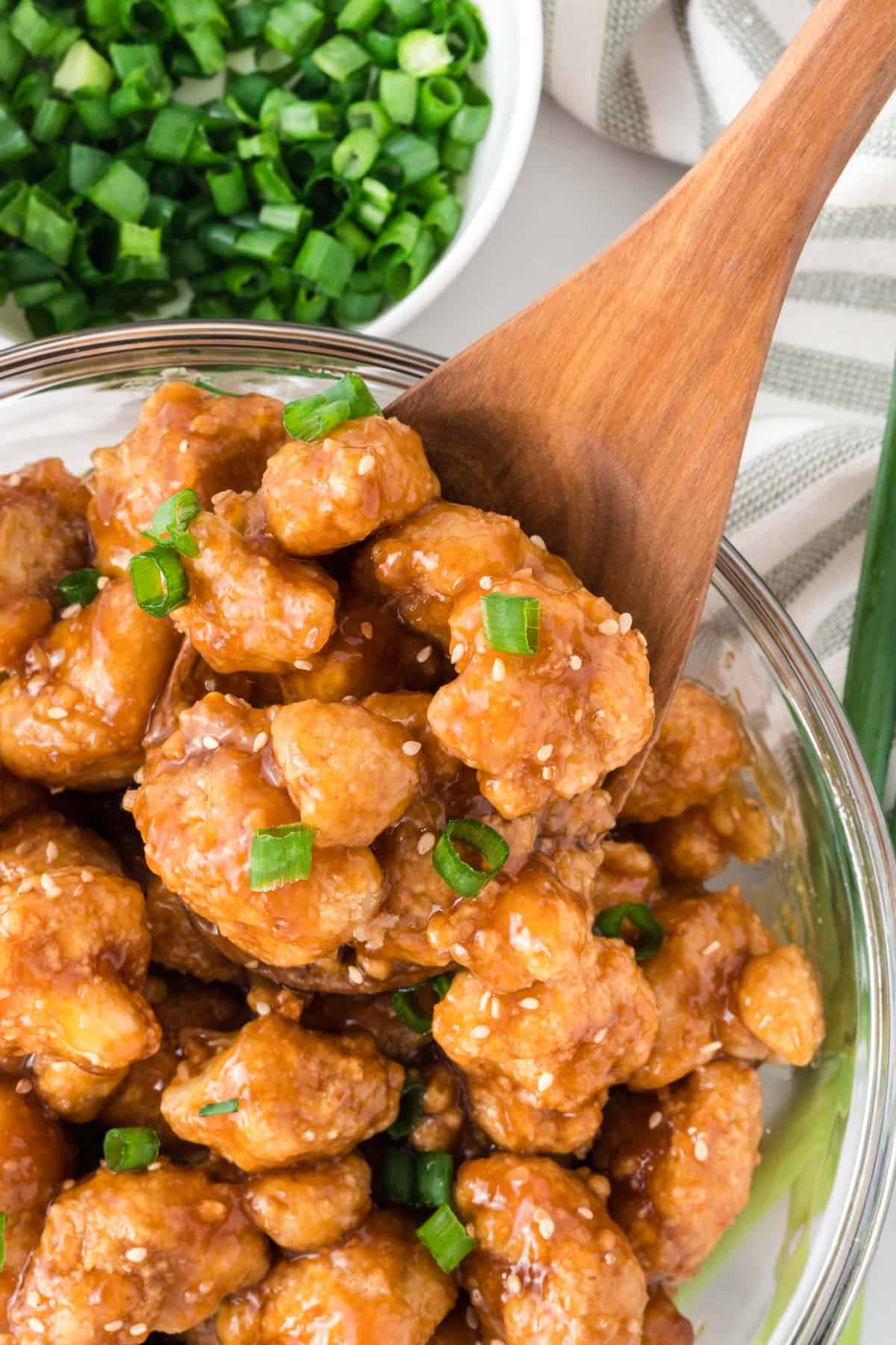 teriyaki cauliflower in a bowl topped with green onions and sesame seeds