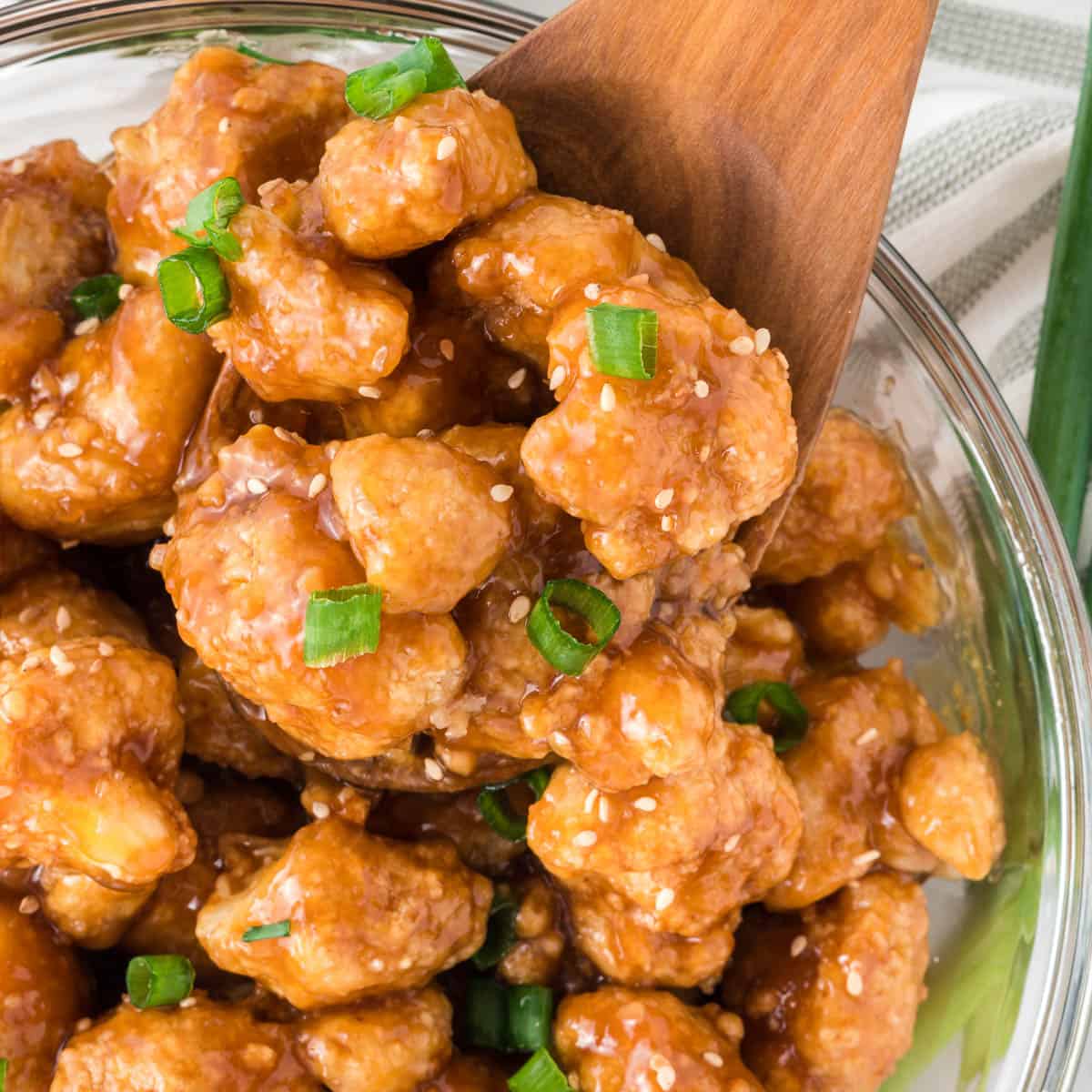 teriyaki cauliflower in a bowl topped with green onions and sesame seeds