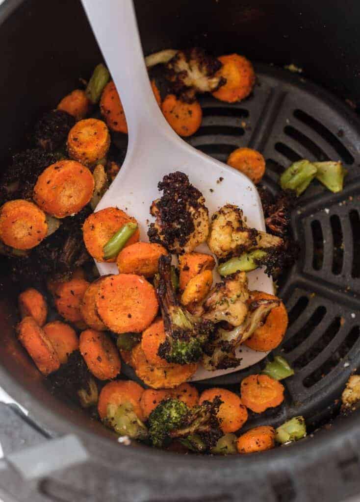 a white spatula taking a scoop of frozen air fried vegetables from the basket