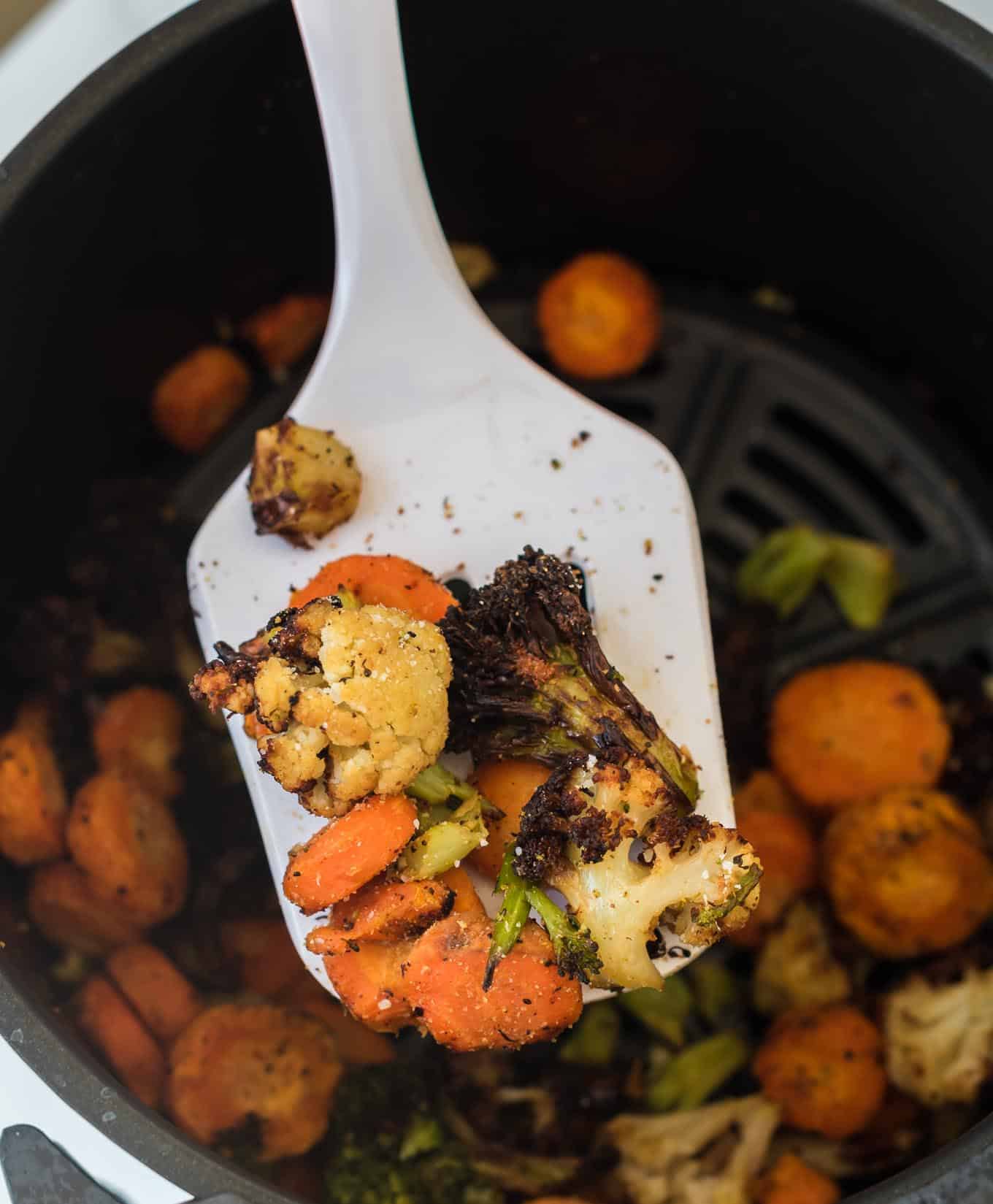 a white spatula taking a scoop of frozen air fried vegetables from the basket