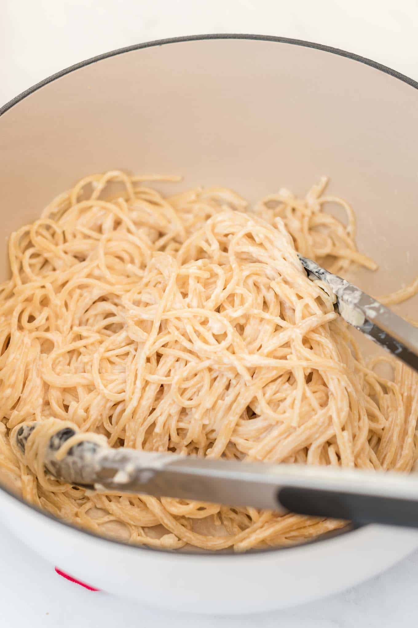 cream cheese pasta in a white dutch oven with tongs