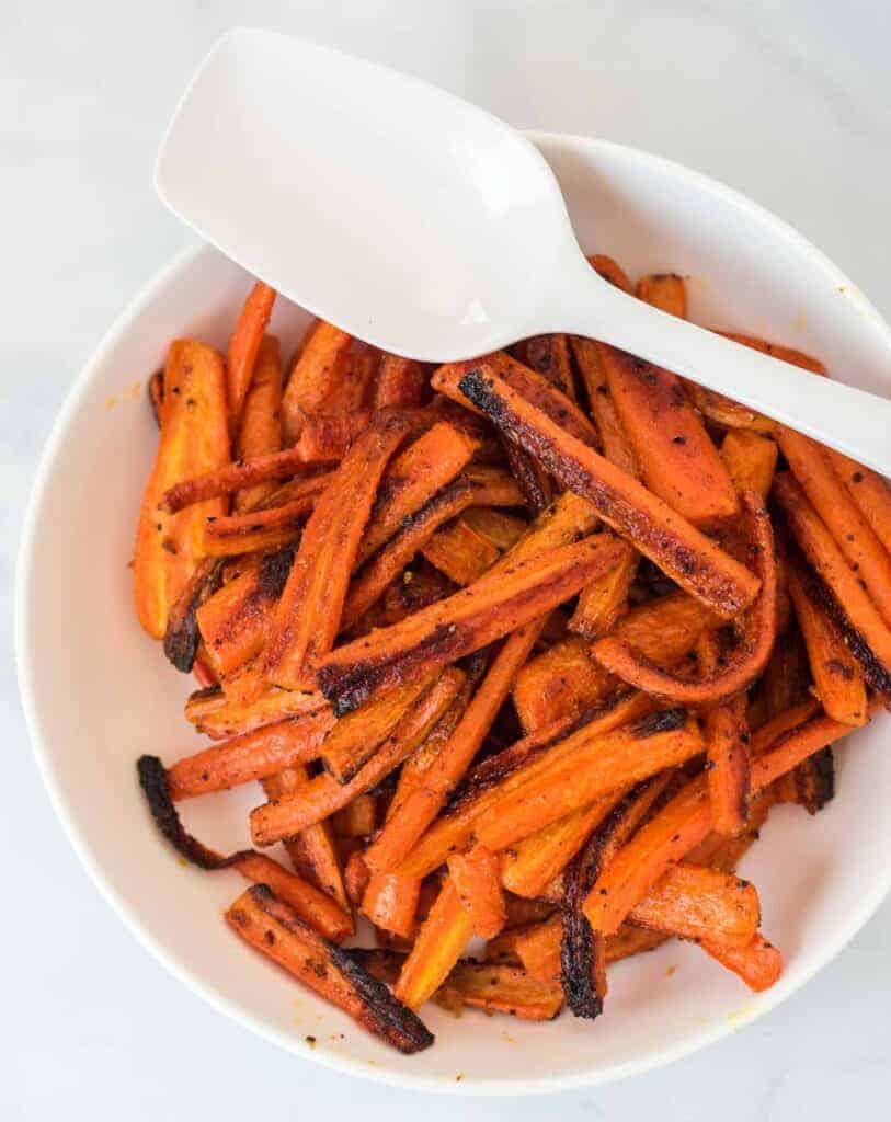 roasted carrots in a white bowl with a spoon