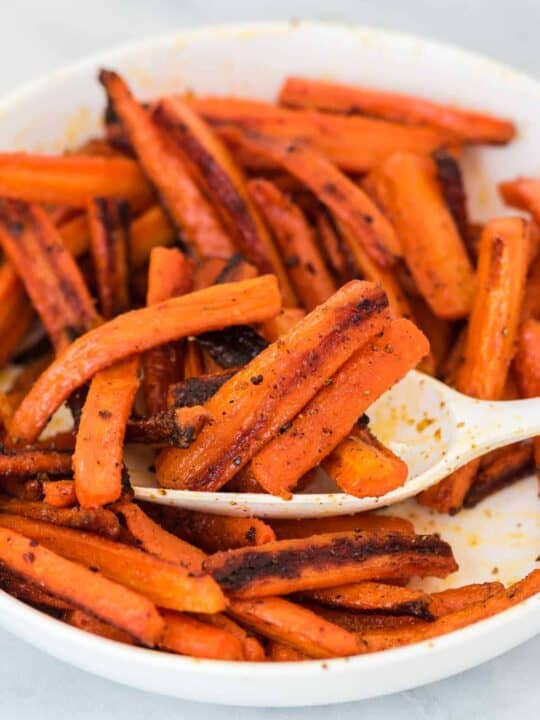 a spoon scooping roasted carrots from a bowl