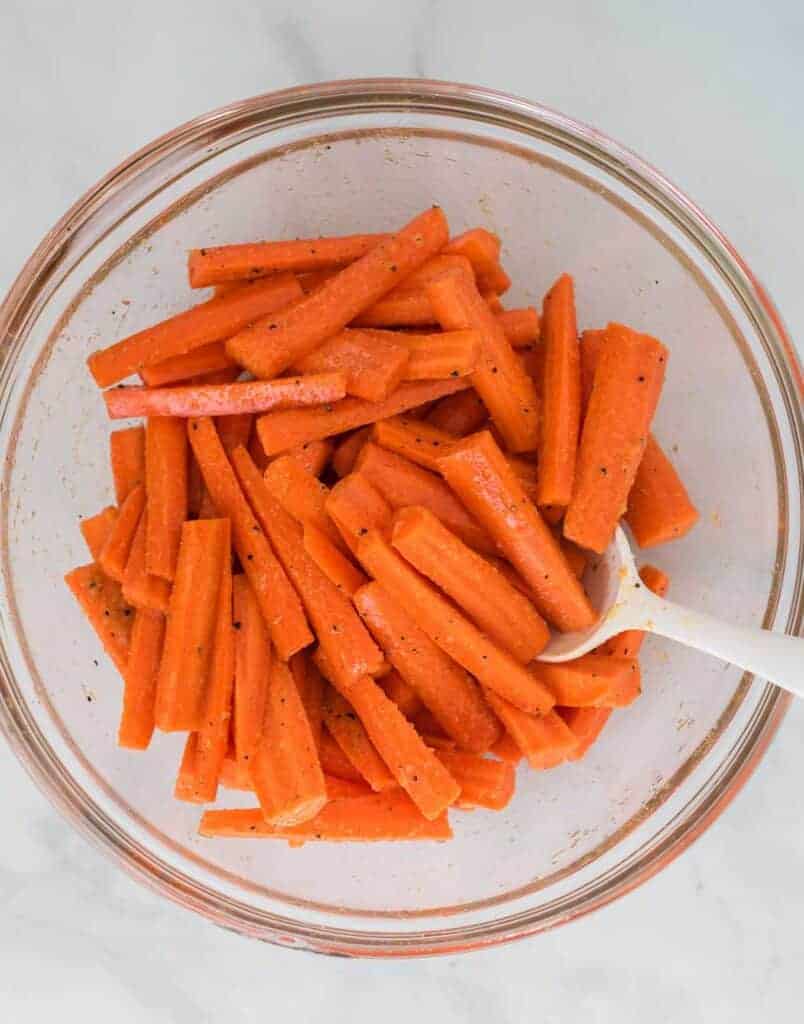 raw carrots tossed with olive oil and spices in a bowl