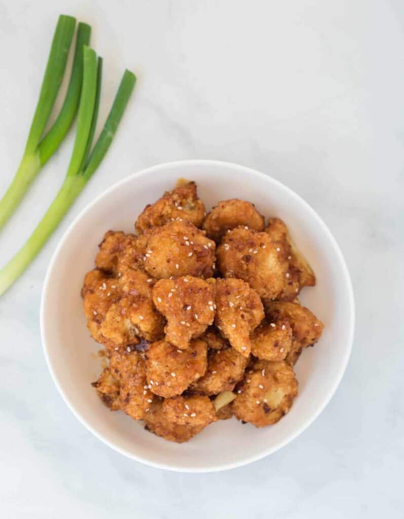 teriyaki cauliflower in a bowl with green onions on the side