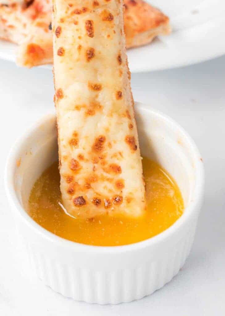 cheese stick being dipped in garlic sauce