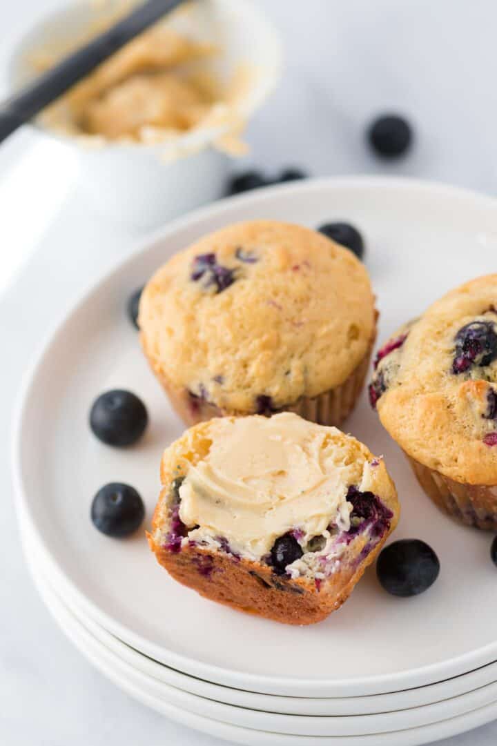 half of a blueberry muffin with honey butter on top with two muffins beside it