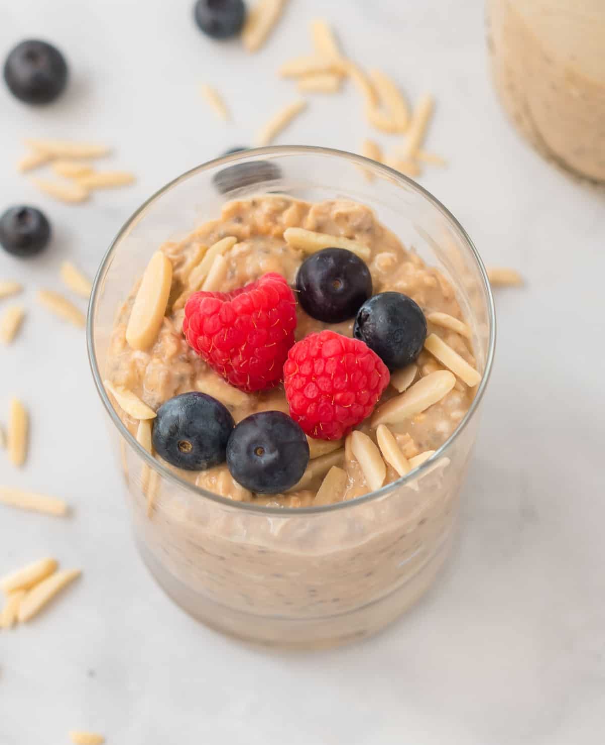 protein overnight oats in a clear glass topped with slivered almonds, raspberries, and blueberries