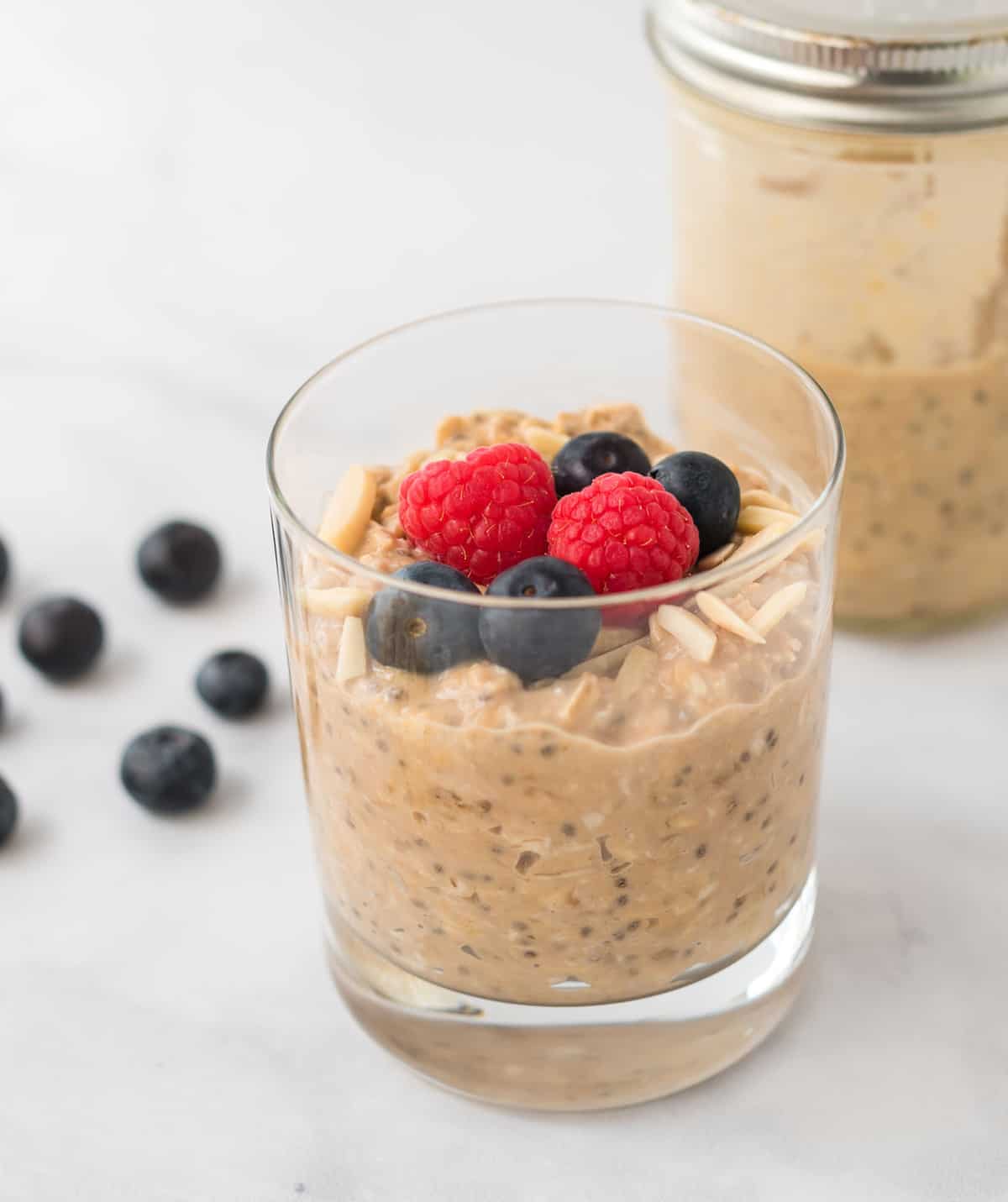 protein overnight oats in a clear glass topped with slivered almonds, raspberries, and blueberries