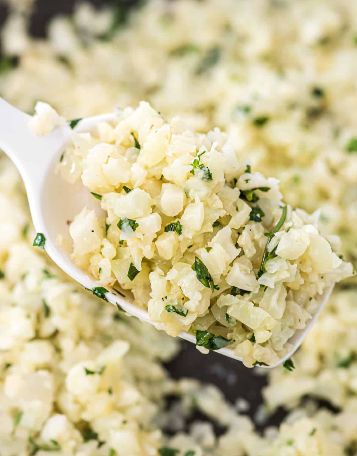 a white spoon taking a scoop of cauliflower rice from the skillet
