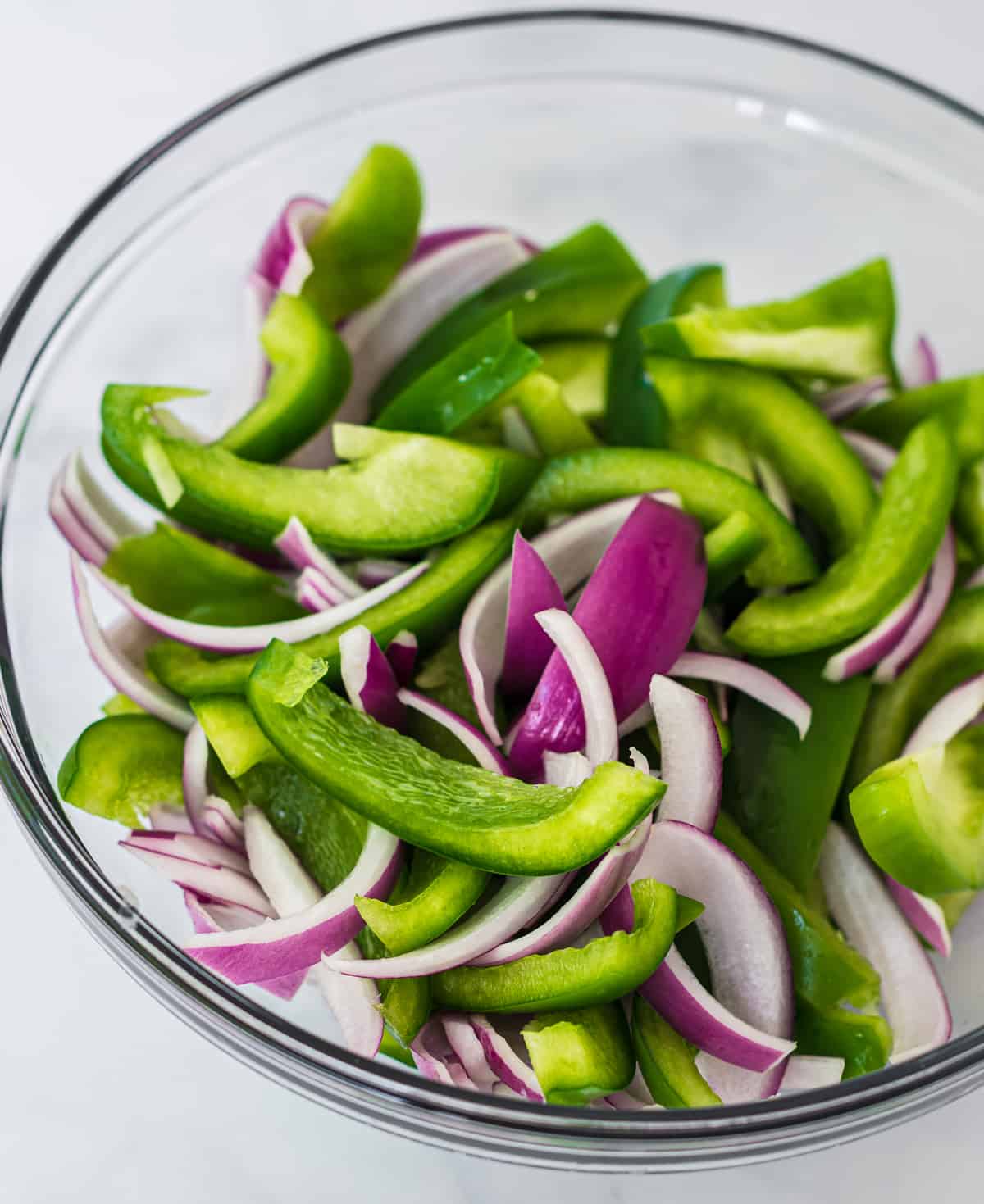 raw sliced green bell pepper and red onion in a glass bowl