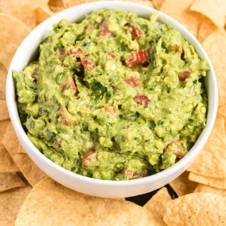 guacamole with tomatoes in a serving bowl surrounded by tortilla chips