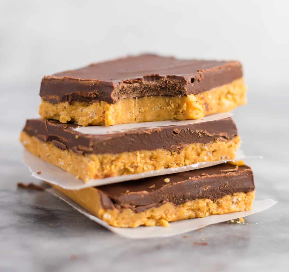 no bake chocolate peanut butter bars stacked between pieces of wax paper