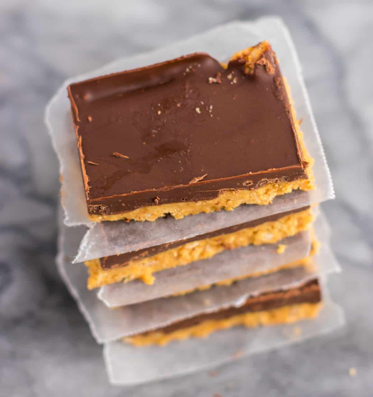 no bake chocolate peanut butter bars stacked between pieces of wax paper