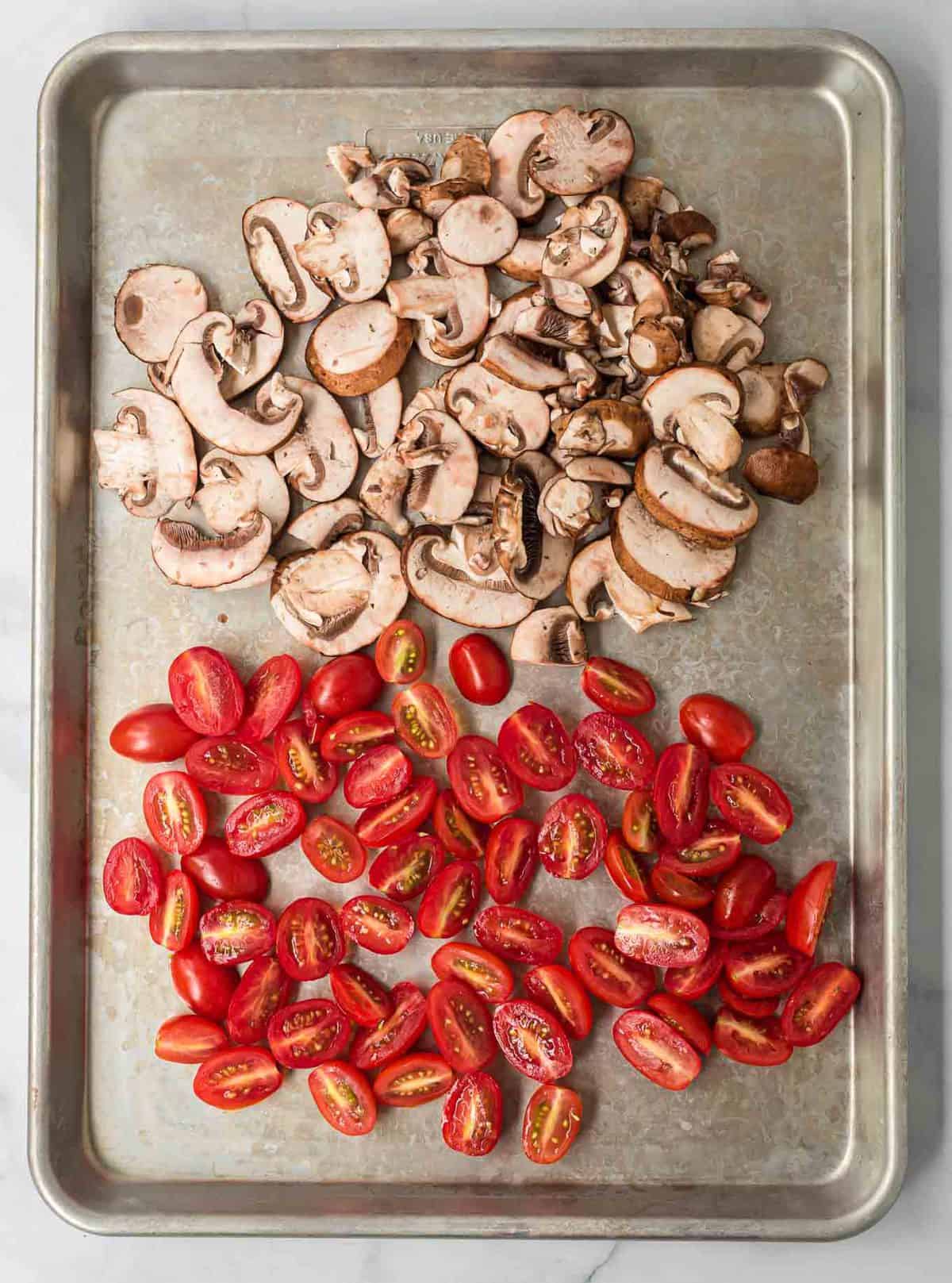 sliced mushrooms and halved cherry tomatoes on a baking sheet