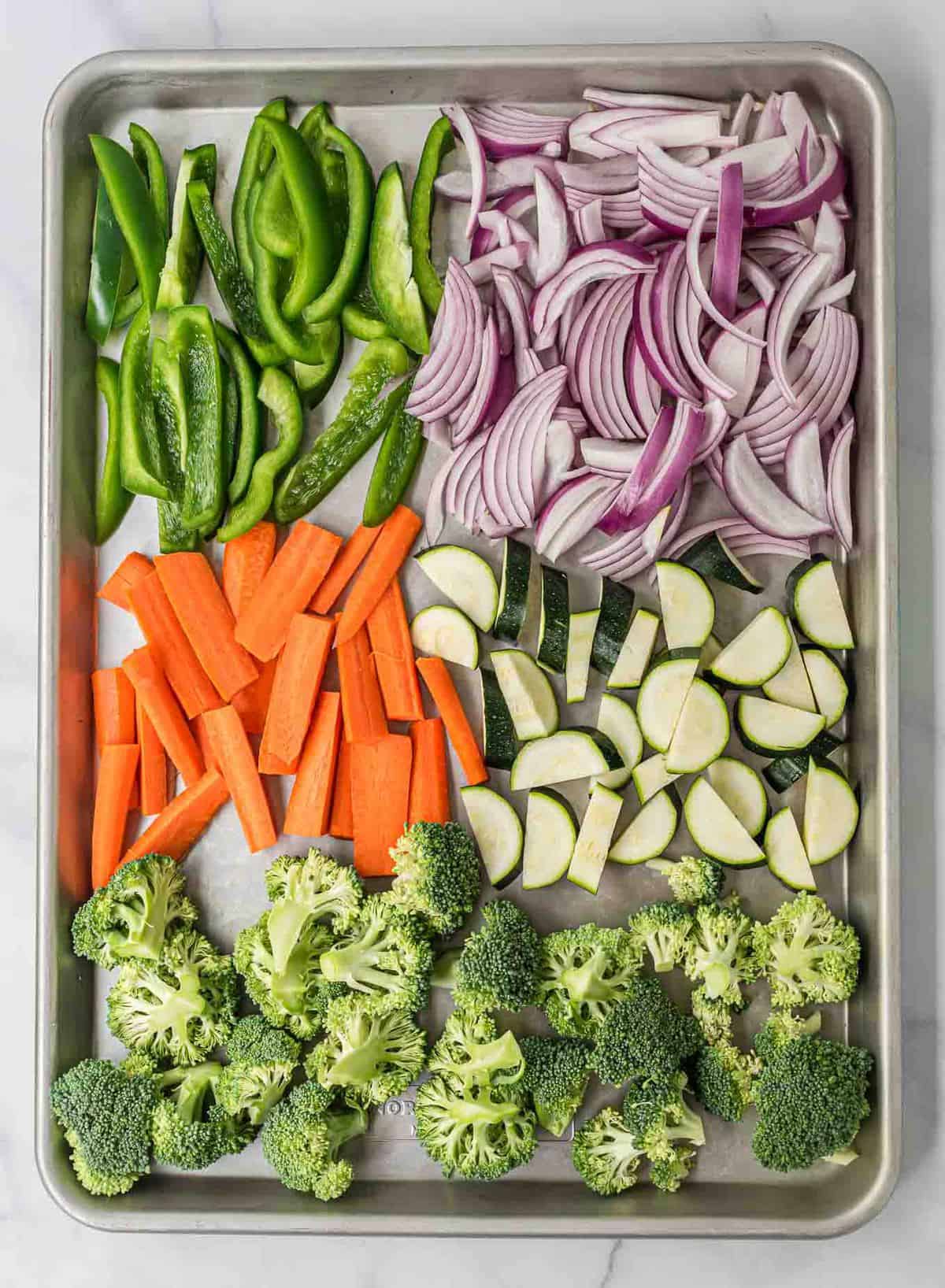 bell peppers, red onion, carrots, zucchini, and broccoli on a baking sheet