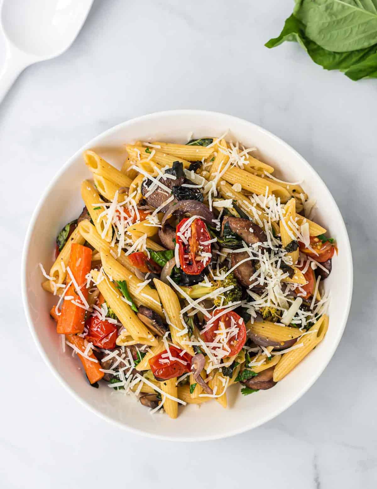 roasted vegetable pasta in a white bowl topped with parmesan cheese