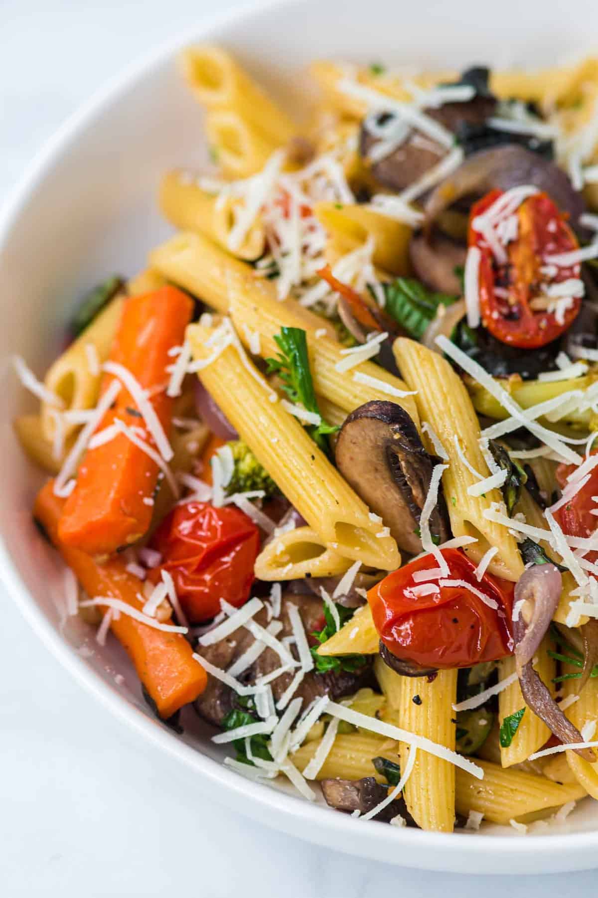 roasted vegetable pasta in a white bowl topped with parmesan cheese