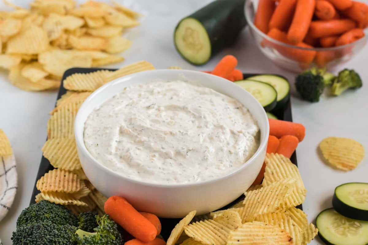 chip dip in a bowl surrounded with cut up vegetables and chips