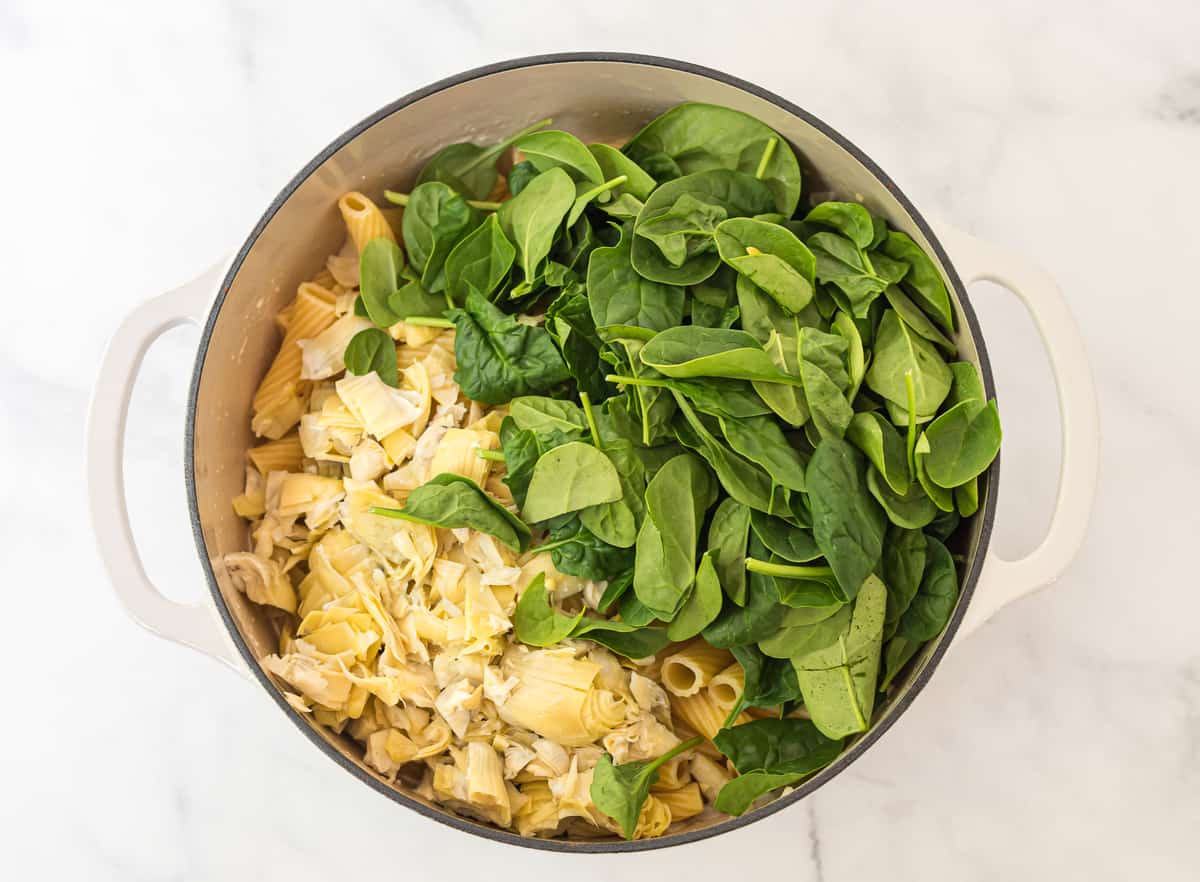 white dutch oven with rigatoni topped with chopped artichokes and spinach