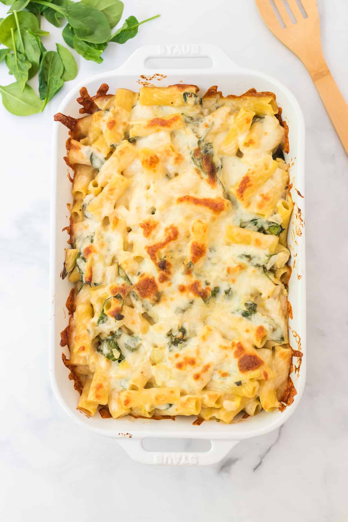 spinach artichoke pasta bake in a white baking dish