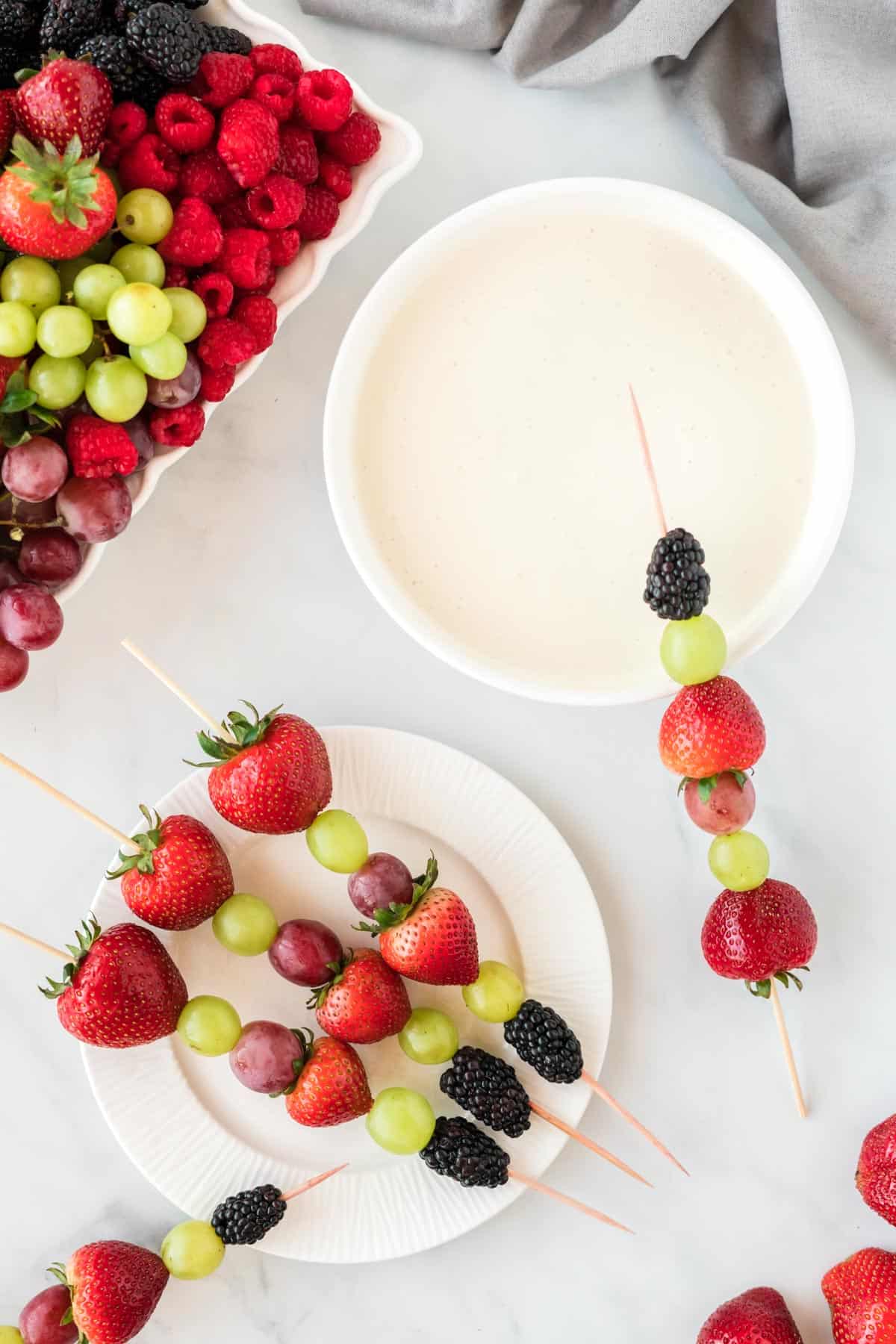 fruit skewers with strawberries, grapes, and blackberries with a bowl of fruit dip