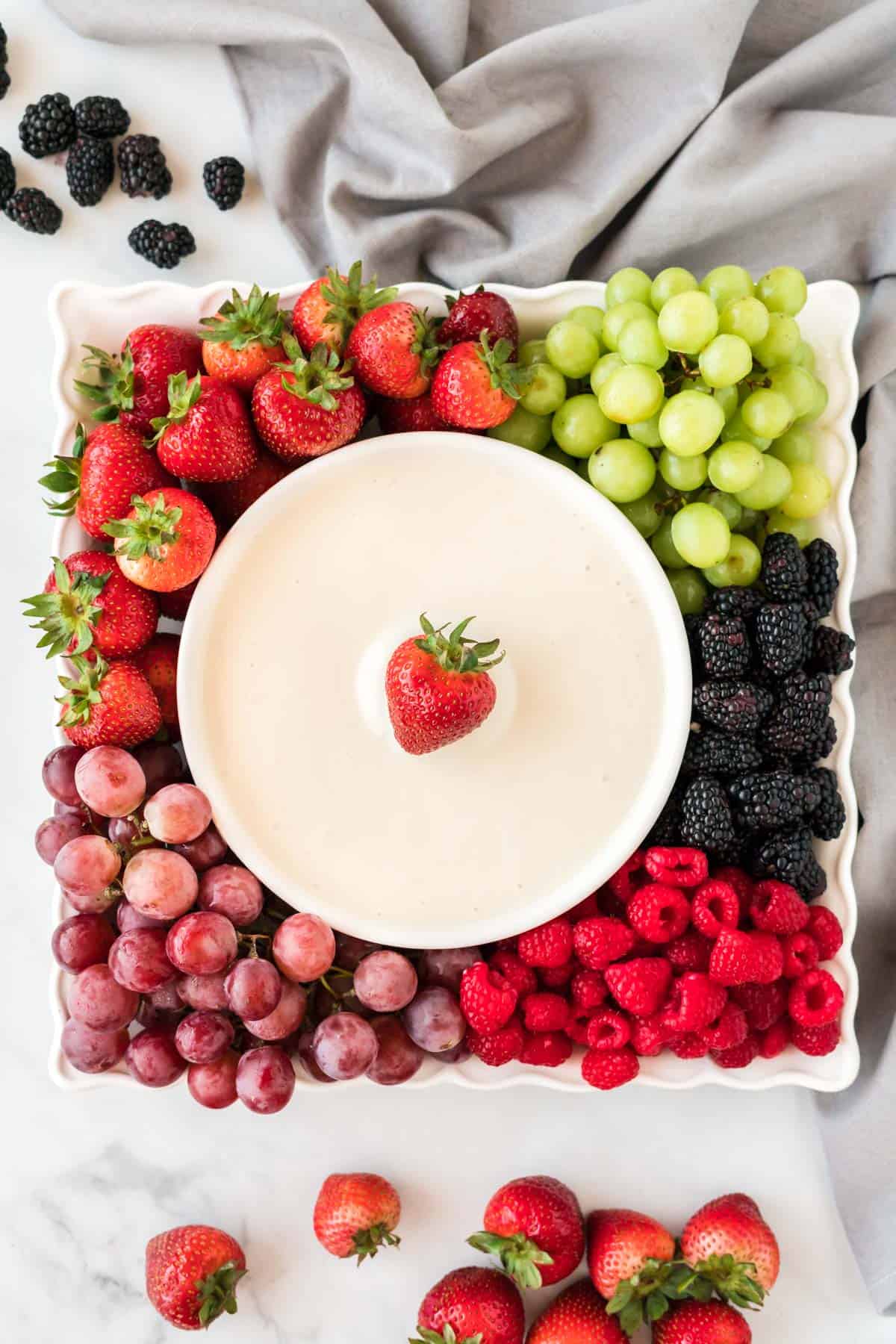 cream cheese dip in a bowl surrounded by fresh fruit on a platter
