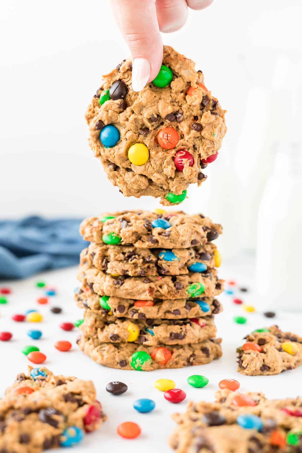 a hand taking a monster cookie from a stack of cookies