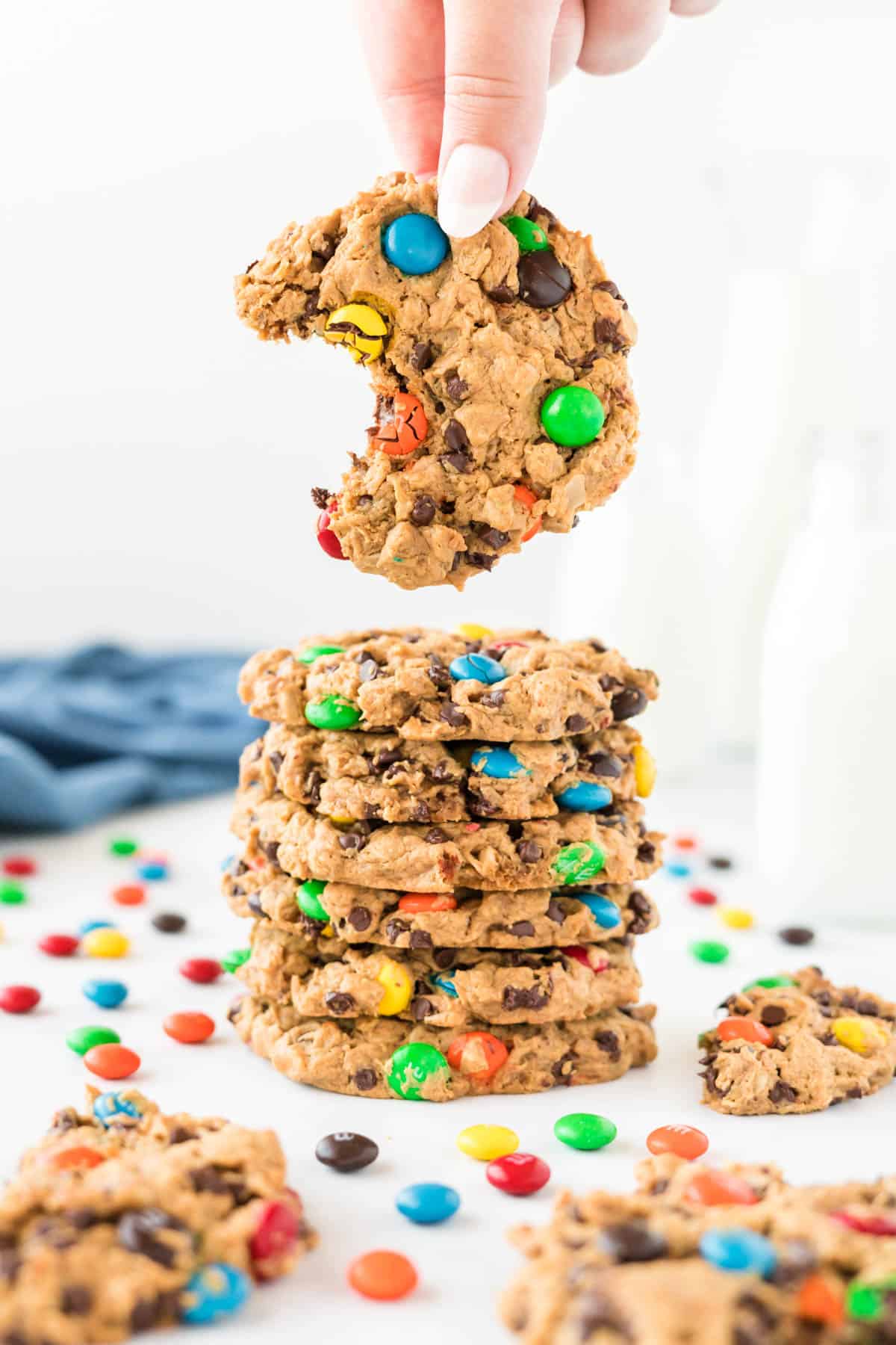 a hand taking a monster cookie with a bite out of it from a stack of cookies