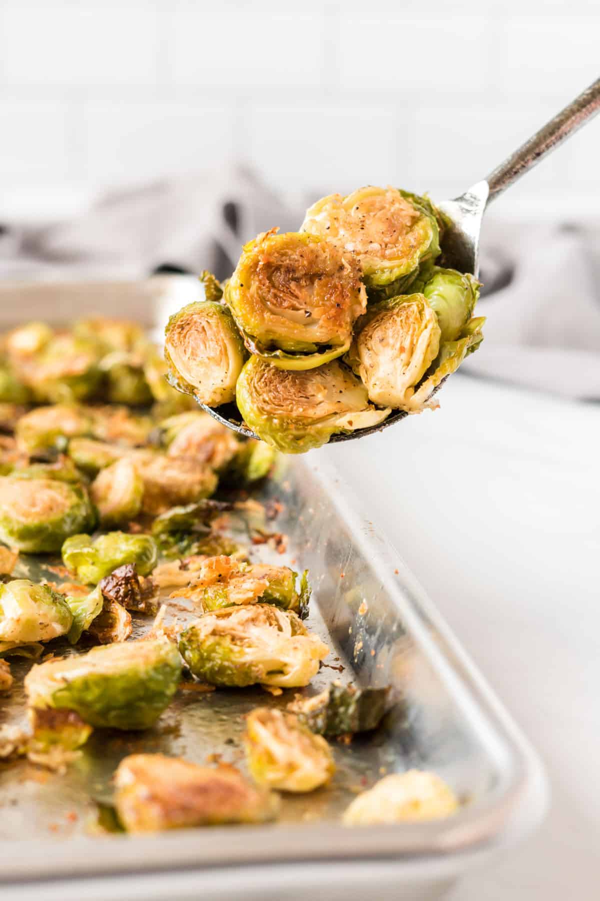 serving spoon taking a scoop of roasted brussel sprouts with parmesan from the baking sheet