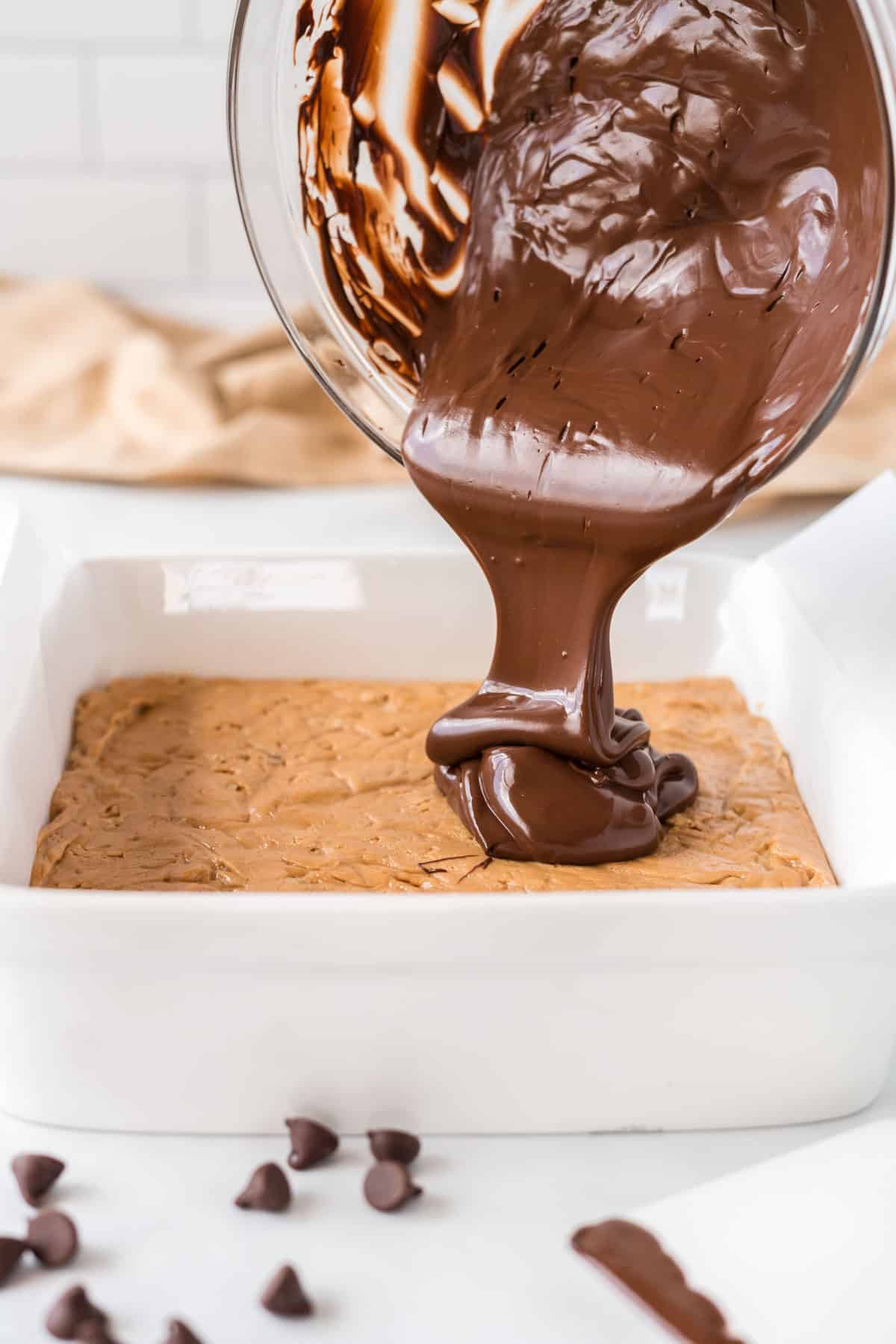 pouring the melted chocolate over the top of the protein bar filling