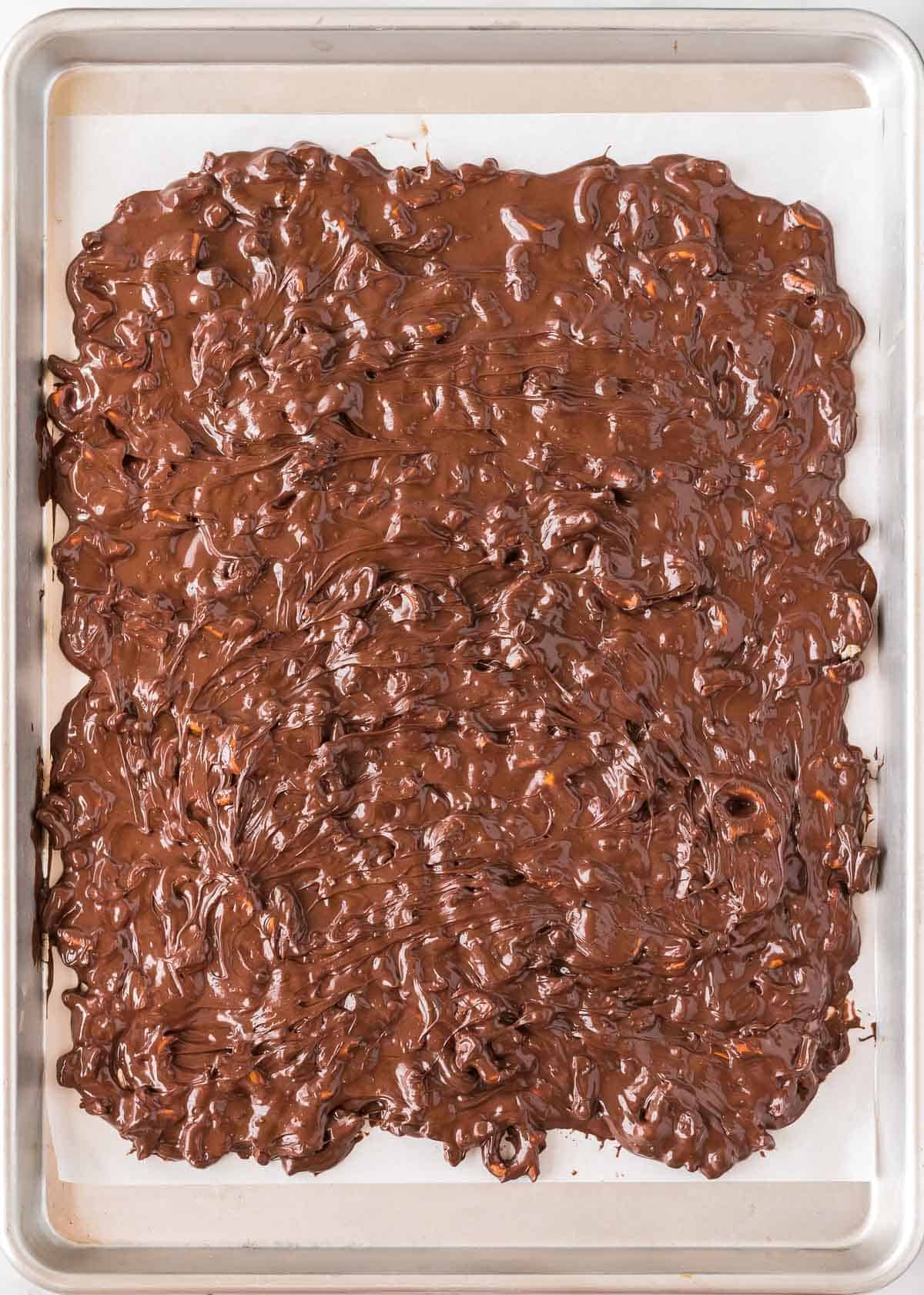 melted chocolate and pretzels spread out on a baking sheet