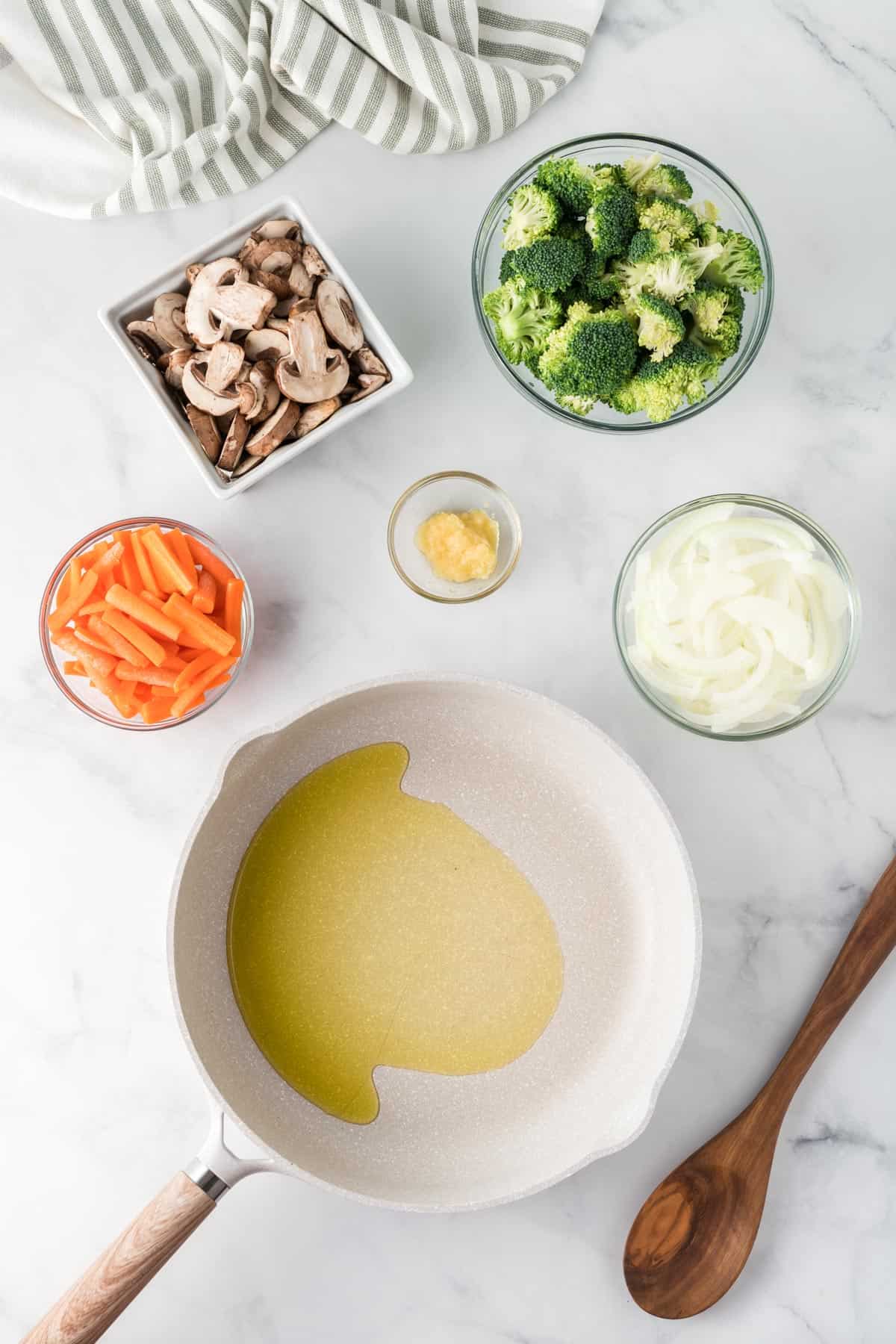 oil in a skillet with bowls of vegetables around it