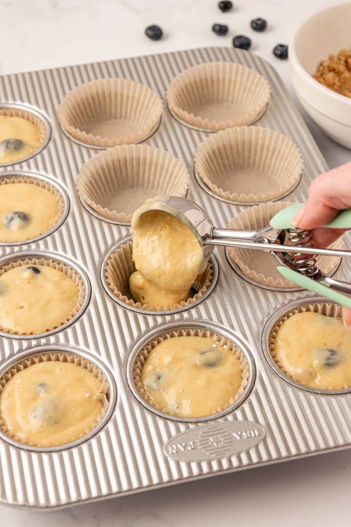 scooping blueberry muffin batter into a muffin tin