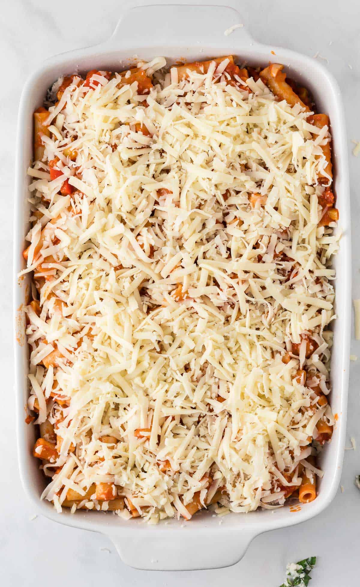 topping the baked ziti with shredded mozzarella