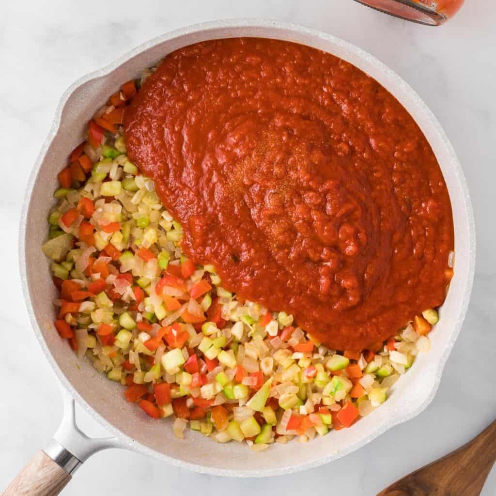 adding the pasta sauce to the cooked vegetables