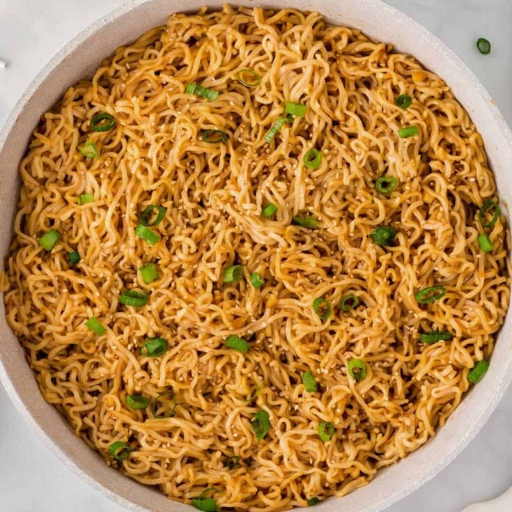 garlic ramen noodles in a skillet topped with green onions