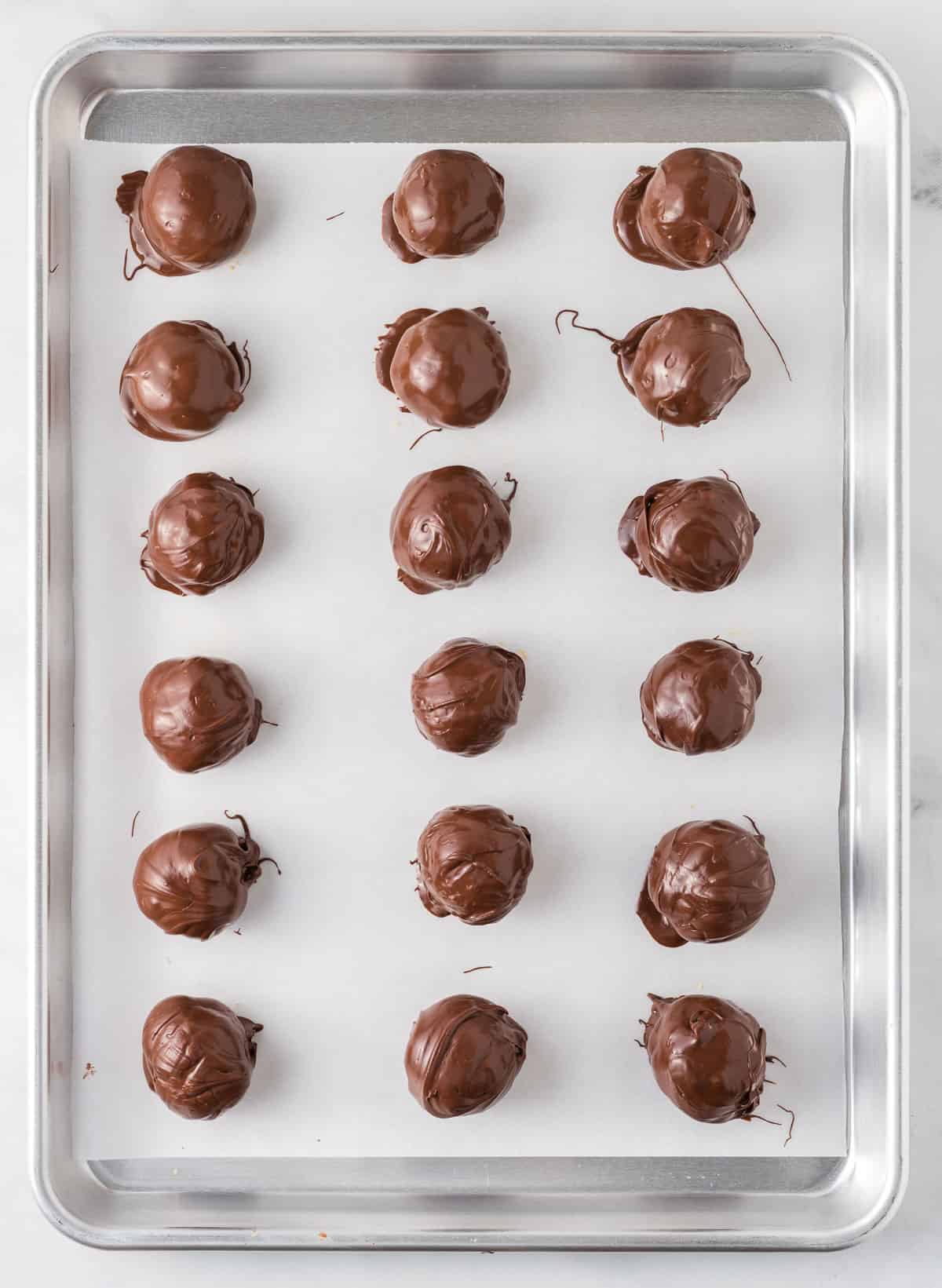 chocolate dipped peanut butter balls on a baking sheet