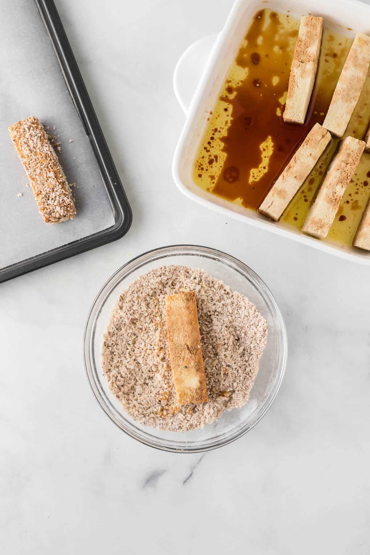 marinated tofu strip being dipped into breading